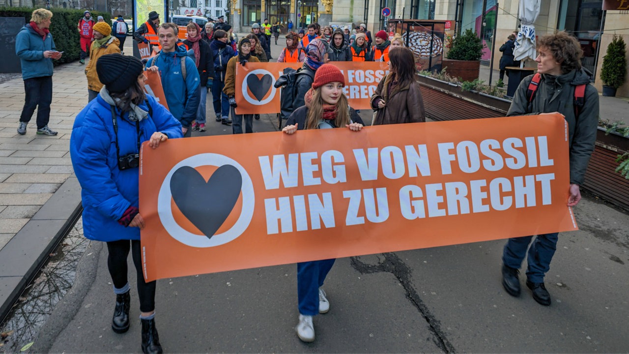 Demenonstranten der "Letzten Generation" tragen ein Banner mit der Aufschrift "Weg von Fossil — Hin zu gerecht" vor sich her.